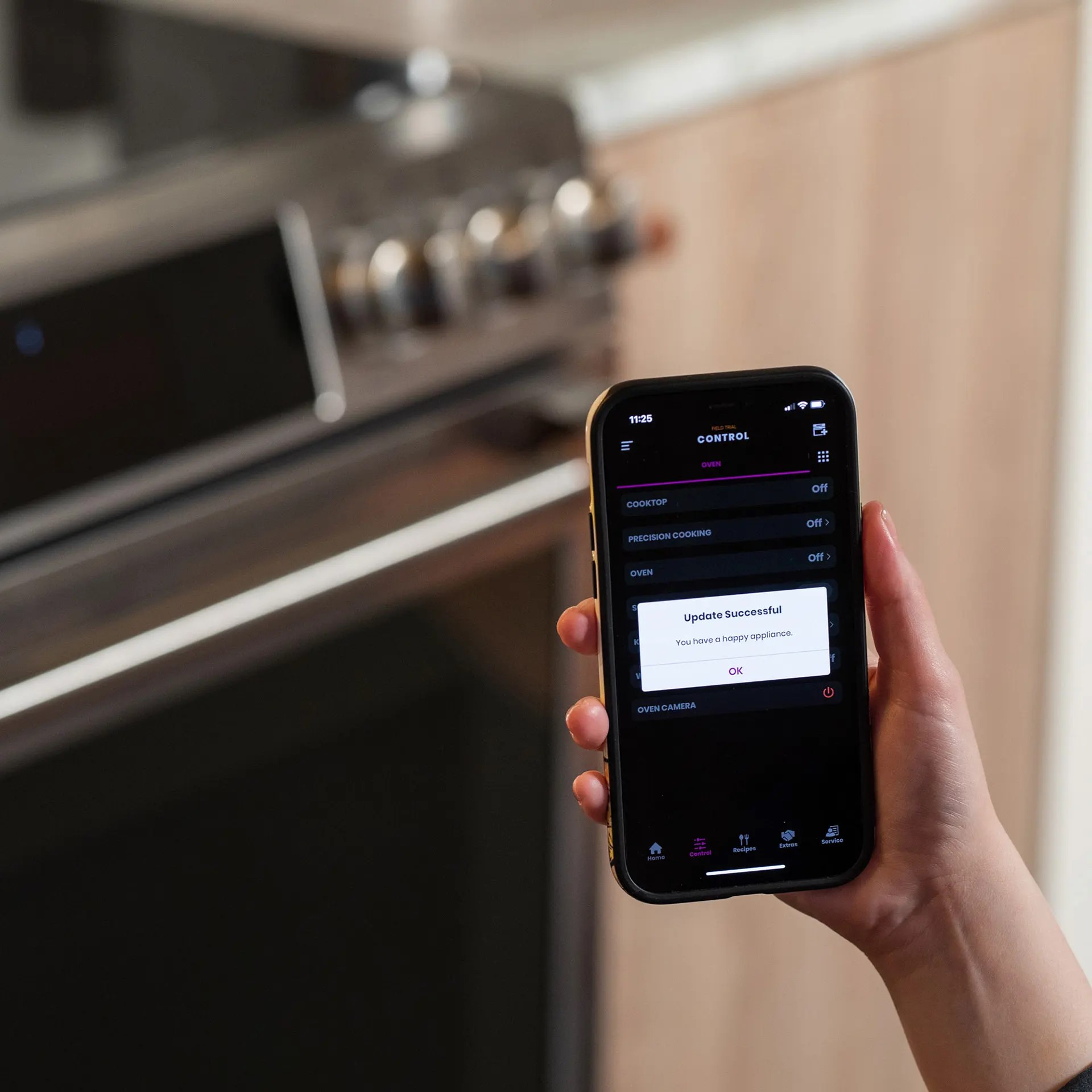 Hand holding a smart phone in front of a Cafe range. The phone display shows an app with 